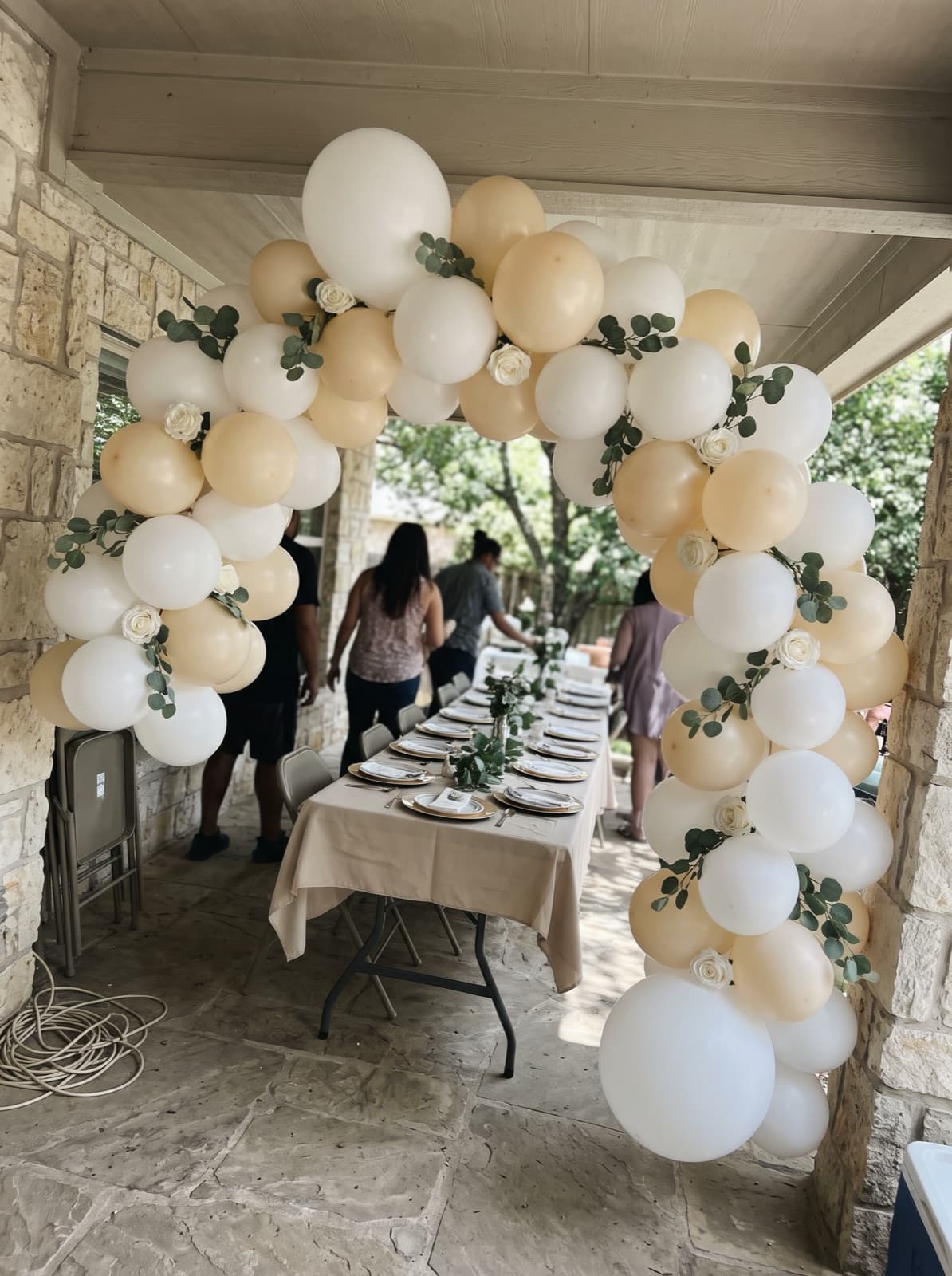 Ivory floral balloon arch with eucalyptus over a patio brunch table