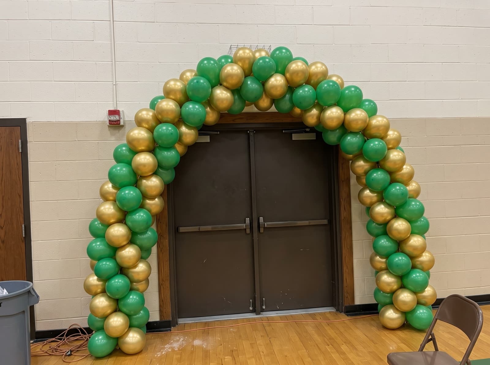 Spiral balloon arch in green and gold over a gym entrance